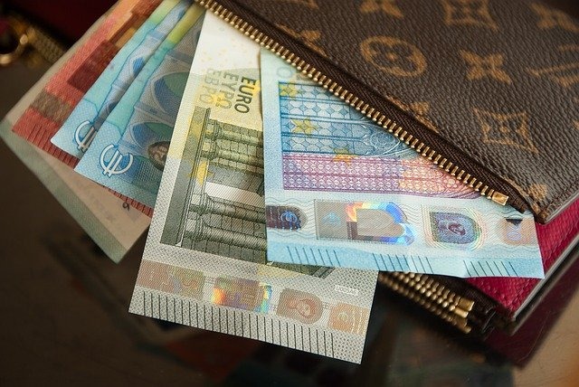 Euro banknoty wystające z brązowego, markowego portfela z widocznym zamkiem błyskawicznym, leżące na błyszczącej powierzchni.