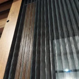 Ciemna, plisowana siatka ochronna na drewnianej ramie okiennej, widok od dołu pod kątem.