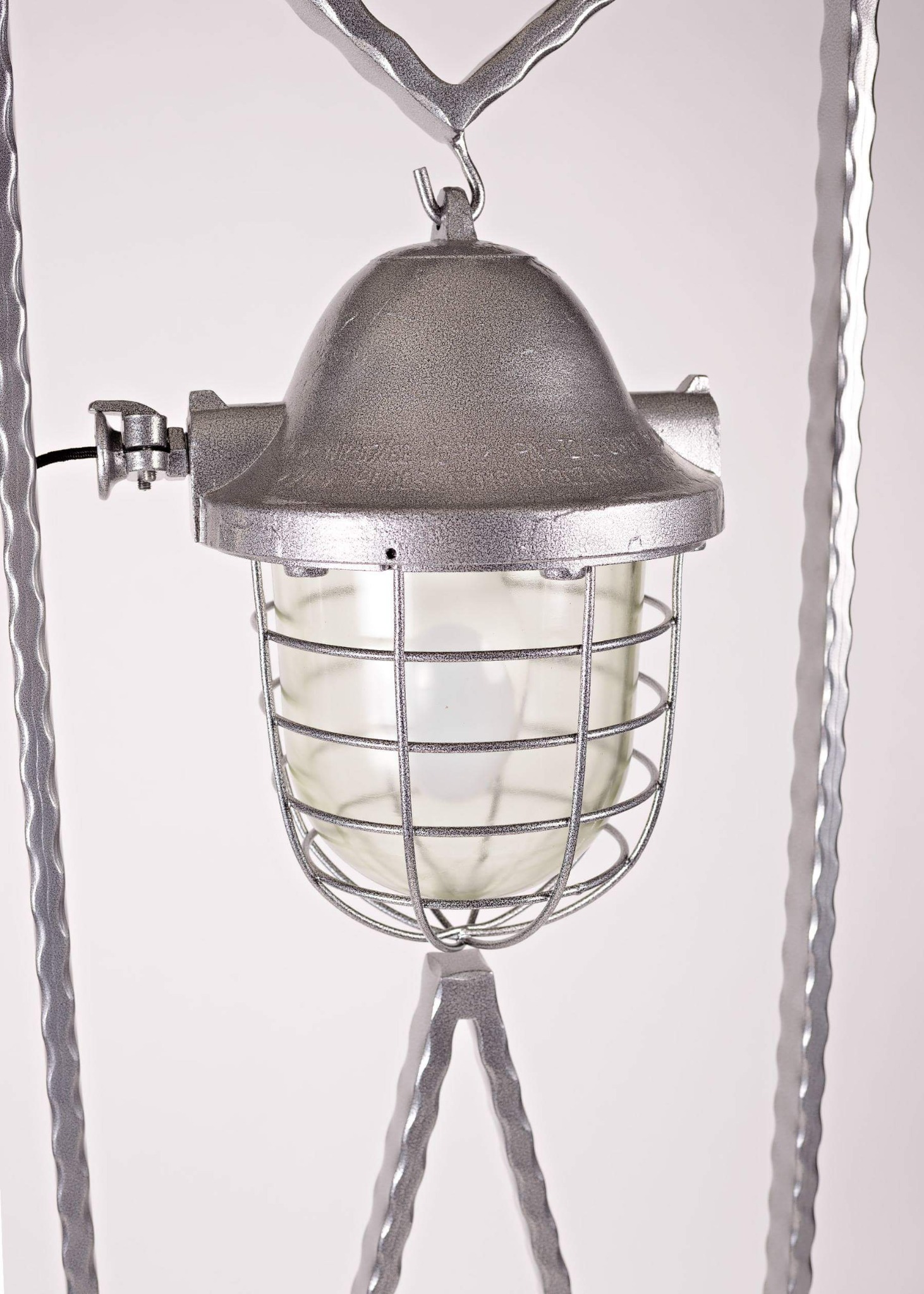 Metalowa lampa stojąca w stylu industrialnym z klatką ochronną żarówki i ozdobnymi nogami.