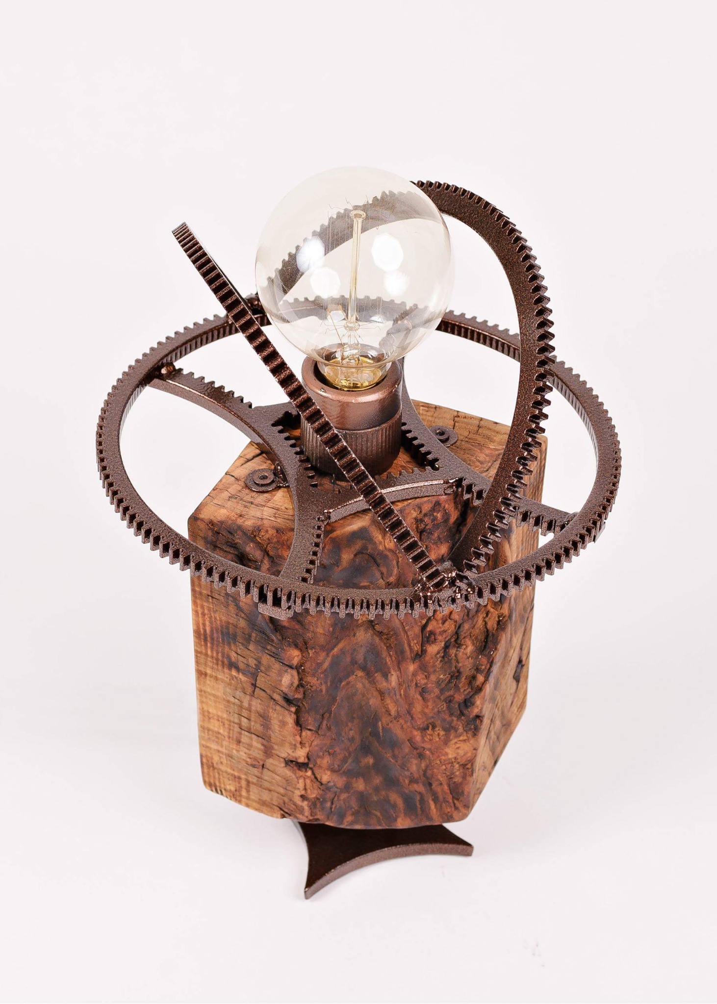 Lampa stołowa w stylu industrialnym: żarówka otoczona metalowymi zębatkami na drewnianej podstawie w kształcie kostki.