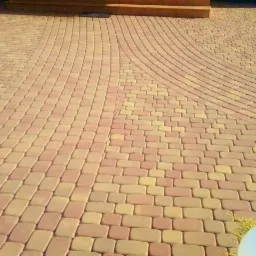 Ułożona z dwukolorowej kostki betonowej ścieżka w ogrodzie, z widocznym obrzeżem i fragmentem trawnika.