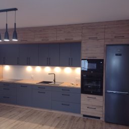 A.W.REM - Nowoczesna kuchnia z szarymi szafkami dolnymi i drewnopodobnymi górnymi, czarnym zlewem i sprzętem AGD marki Beko, oświetlona punktowymi lampami podszafkowymi, z podłogą imitującą drewno.