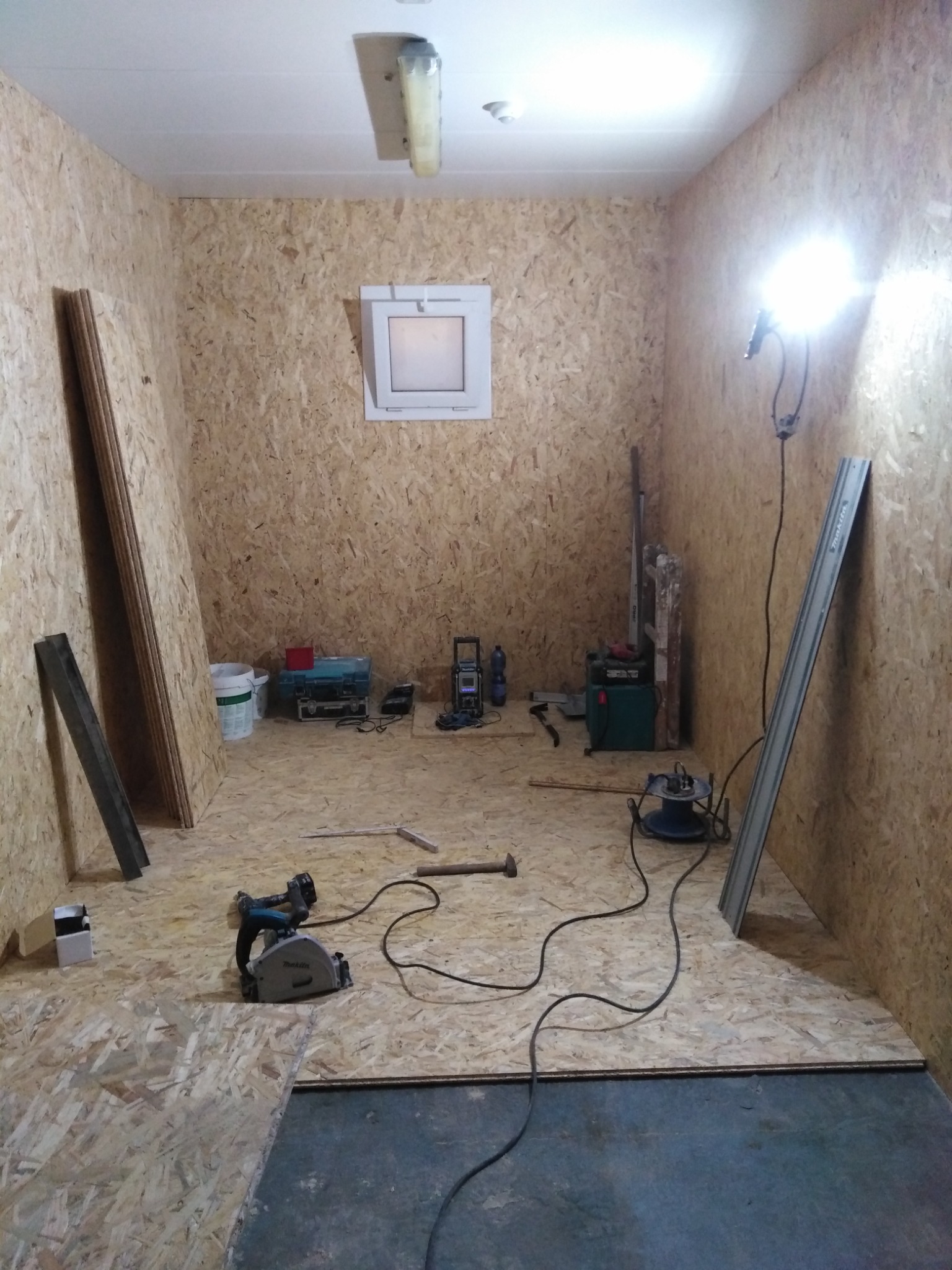 Montaż płyt OSB na podłodze w Luboszycach, widoczna piła tarczowa Makita, płyty na ścianach i podłodze, surowe wnętrze w trakcie prac wykończeniowych.