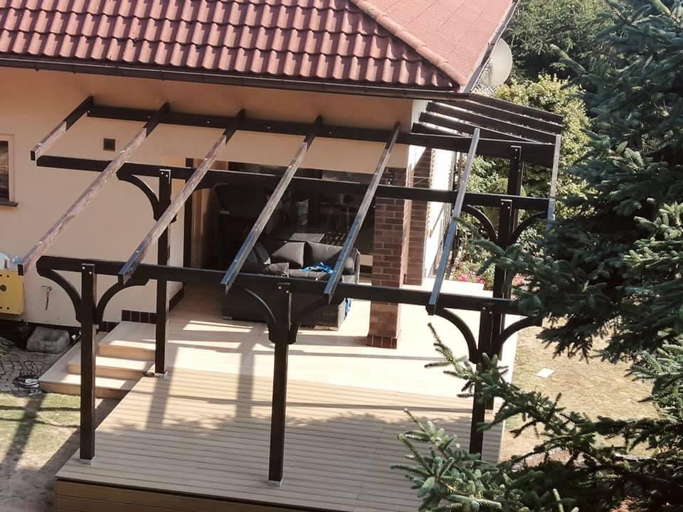 Zadaszenie tarasu z drewnianą konstrukcją w trakcie budowy, widoczne elementy więźby i podłoga tarasu z desek kompozytowych.
