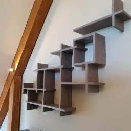 Nietypowa, geometryczna p&oacute;łka ścienna z drewna w odcieniach szarości, zamontowana w pomieszczeniu z drewnianą belką stropową w Czarnogłowach.