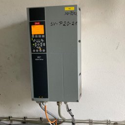 Robert Grochulski - Szary falownik Danfoss VLT Aqua Drive zamontowany na białej ścianie, widoczne podłączenia kablowe w peszlach i korytkach.