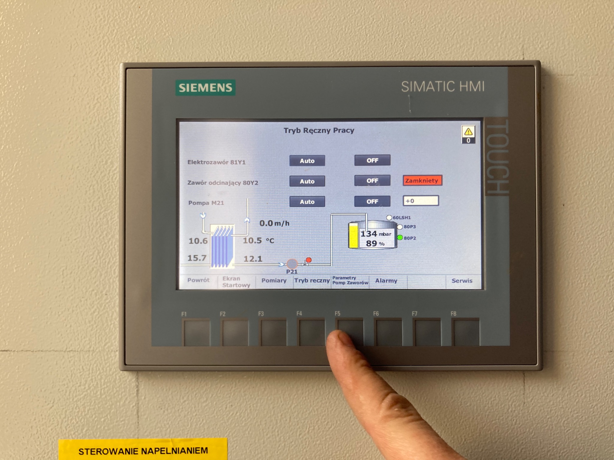 Ekran dotykowy panelu sterowania Siemens SIMATIC HMI z widocznym interfejsem trybu ręcznego pracy, palec wskazujący na przycisk funkcyjny F5, żółta naklejka 'STEROWANIE NAPELNIANIEM' w dolnym rogu.