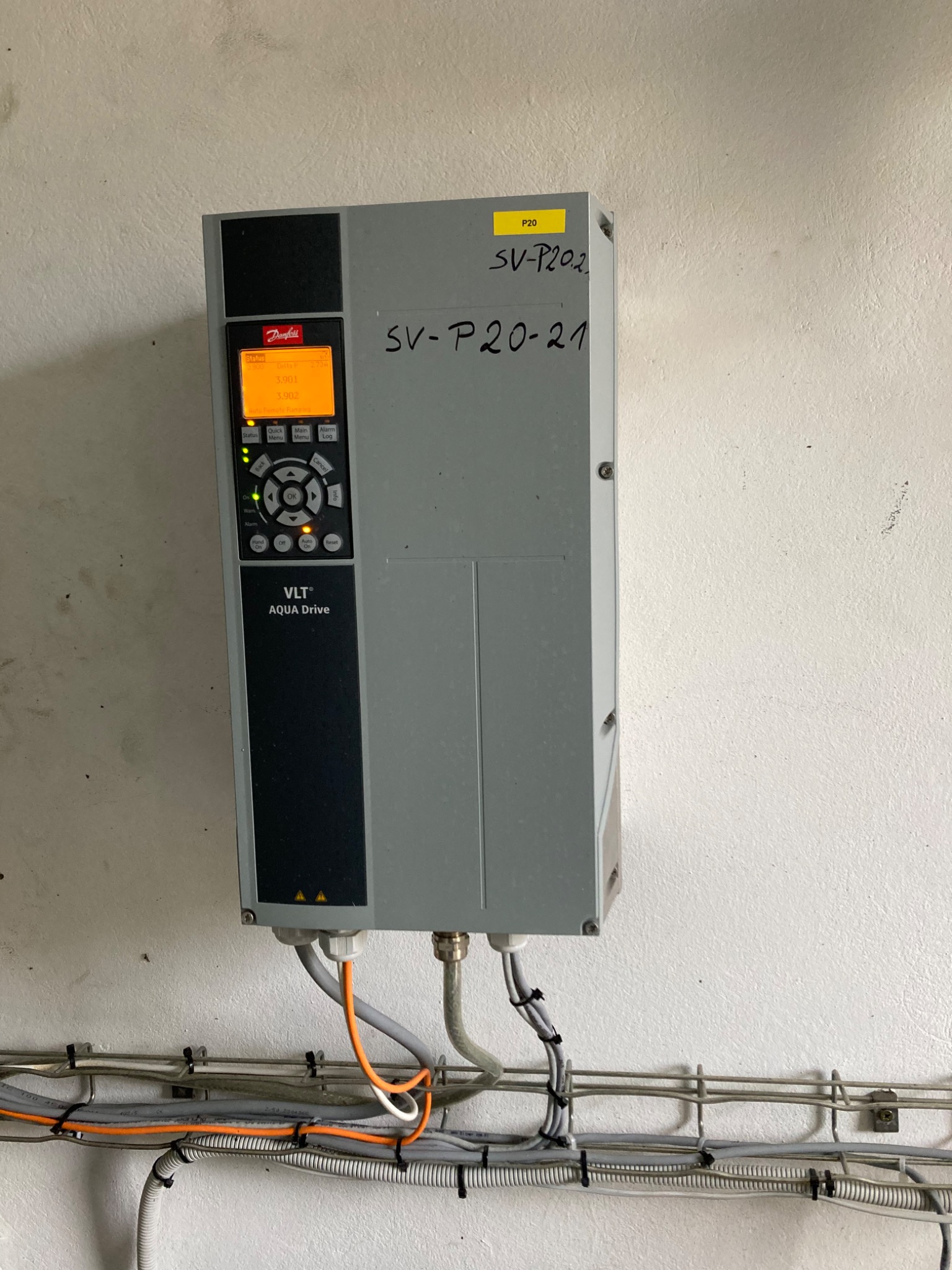 Szary falownik Danfoss VLT Aqua Drive zamontowany na białej ścianie, widoczne podłączenia kablowe w peszlach i korytkach.