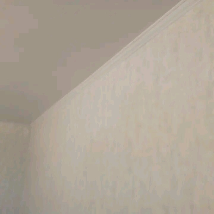 Jasna tapeta w delikatny wzór na ścianie w rogu pokoju, widoczna listwa przysufitowa.