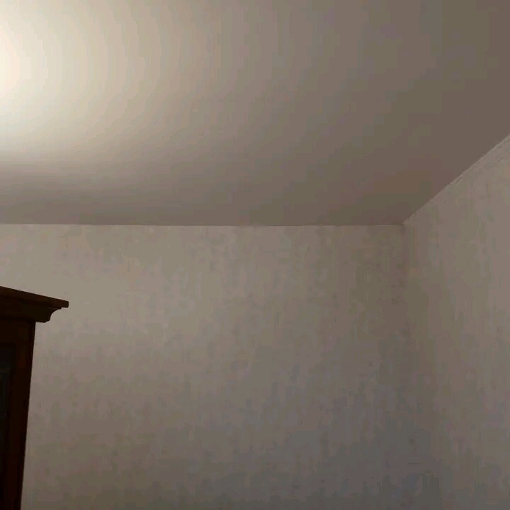 Fragment pokoju po odświeżeniu: gładki, jasny sufit i ściana z delikatną strukturą, widoczny róg pomieszczenia oraz fragment ciemnego mebla w lewym dolnym rogu.
