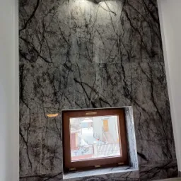 Ściana wyłożona płytami imitującymi marmur z wyraźnym wzorem żyłkowania, z wnęką okienną z drewnianą ramą, oświetlona dwoma punktowymi lampami sufitowymi.