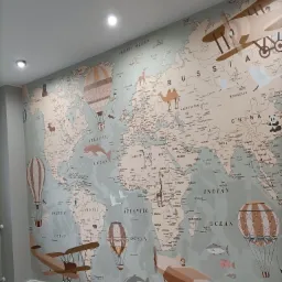 Pok&oacute;j dziecięcy z tapetą przedstawiającą mapę świata z rysunkami samolot&oacute;w i balon&oacute;w, jasnoszara podłoga, neutralne ściany, oświetlenie sufitowe.
