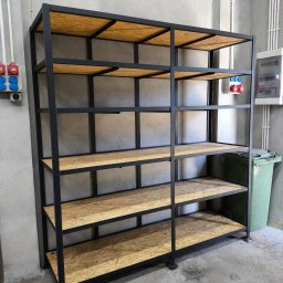 RAF-SPAW RAFAŁ KOPCZYK - Metalowy regał z drewnianymi półkami z płyty OSB, spawane czarne profile, surowe betonowe tło, widoczne gniazda elektryczne i skrzynka rozdzielcza.