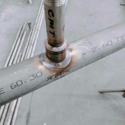 WIKLAR Konstrukcje Stalowe RAFAŁ KOPCZYK - Zbliżenie na spawany element z rury stalowej z widocznym oznaczeniem CMT i numerami seryjnymi, ukazujący precyzyjne połączenie dwóch rur.