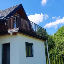 Nowoczesny dom z balkonem zabezpieczonym metalową balustradą, widok z zewnątrz w słoneczny dzień.