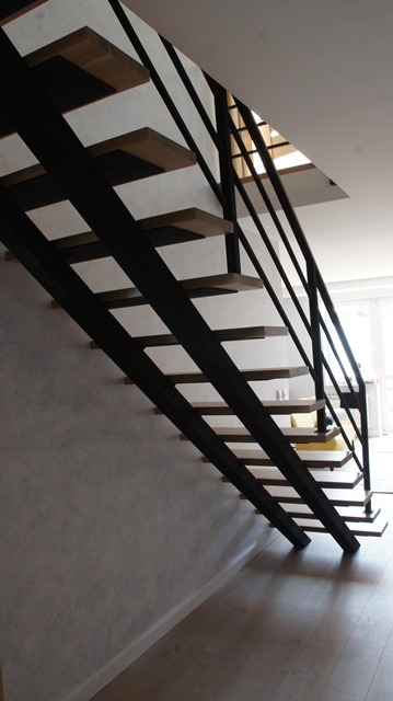 Nowoczesne schody metalowe z drewnianymi stopniami, czarna konstrukcja, minimalistyczny design, widok z dołu, jasne wnętrze.
