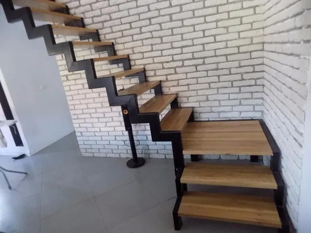 Nowoczesne schody z czarną metalową konstrukcją i drewnianymi stopniami, zamontowane przy ścianie z białej cegły.