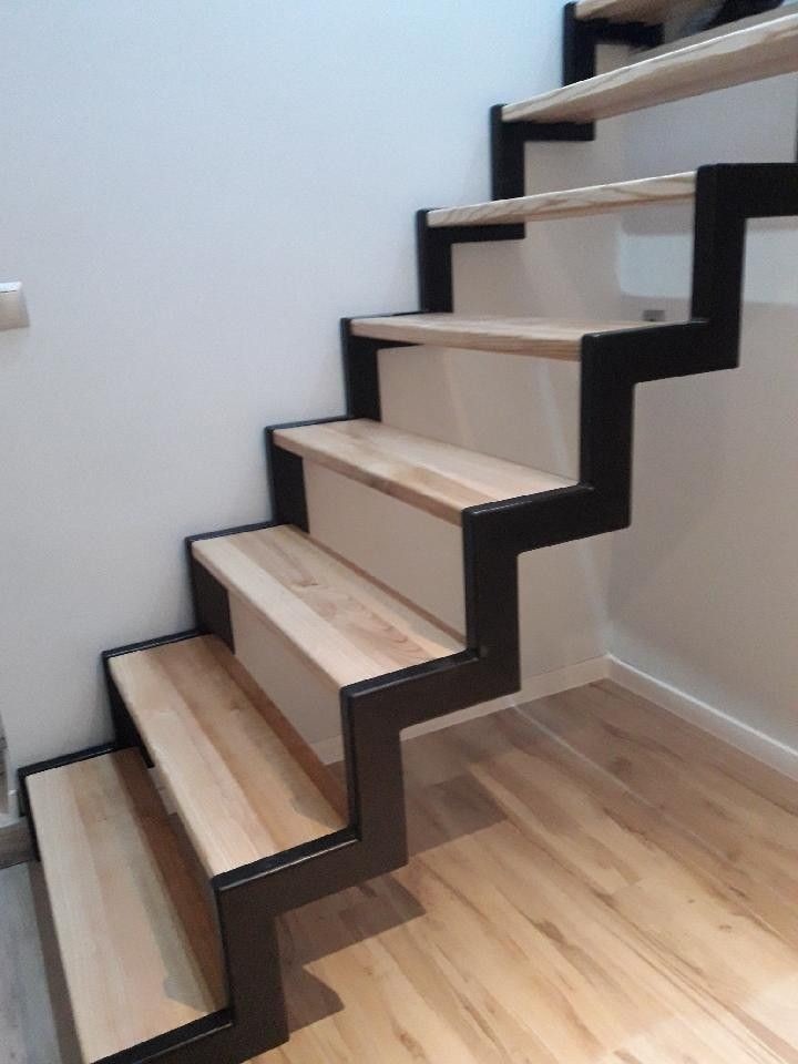 Nowoczesne schody z drewnianymi stopniami i czarną, metalową konstrukcją nośną, widok z dołu na jasną ścianę i podłogę z paneli.