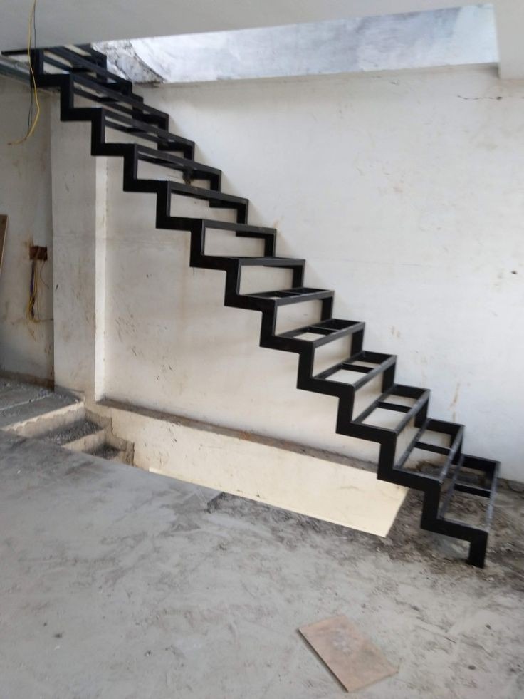 Surowe, czarne metalowe schody bez stopni, przymocowane do surowej, białej ściany w trakcie montażu.