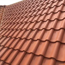 Nowy dach z czerwonej dachówki ceramicznej, widok z góry na fragment połaci dachowej z wyraźnym wzorem ułożenia.