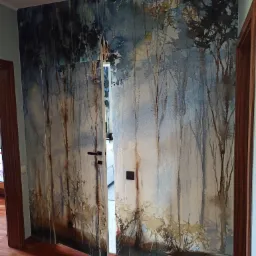 Drzwi przesuwne z fototapetą imitującą akwarelowy las, zamontowane w pokoju z parkietem w odcieniach czerwieni.