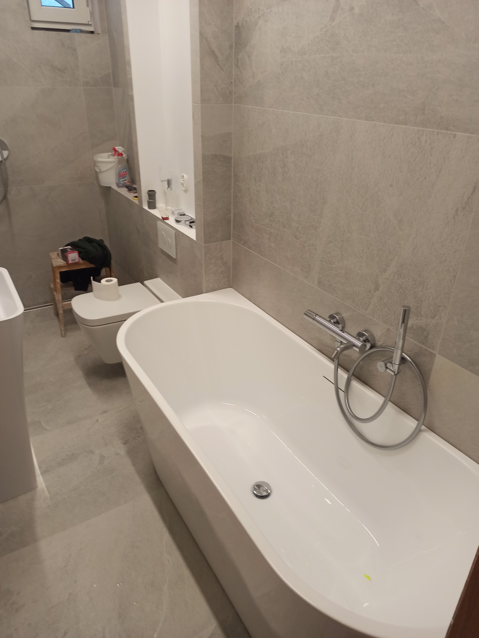 Nowoczesna łazienka z wanną z hydromasażem i szarą, marmurkową glazurą, widoczne narzędzia i akcesoria na półce, toaleta z rolką papieru na desce.