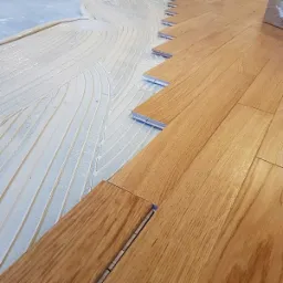 Układanie parkietu z klejem: widok z góry na proces montażu drewnianej podłogi, z widocznymi rowkami na klej i fragmentami parkietu w trakcie łączenia.