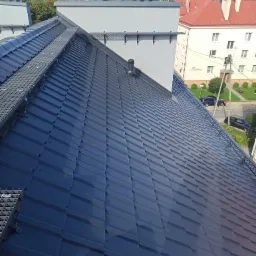 Nowoczesny, ciemnoszary dach z blachy na budynku wielorodzinnym, z zainstalowanymi stopniami kominiarskimi i wentylacją kominową, widok z góry.