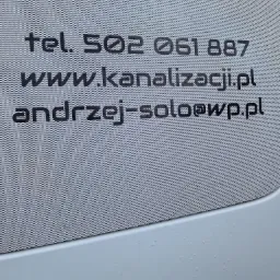 Reklama firmy kanalizacyjnej z numerem telefonu, adresem strony internetowej i adresem e-mail umieszczona na perforowanej folii okiennej na samochodzie.