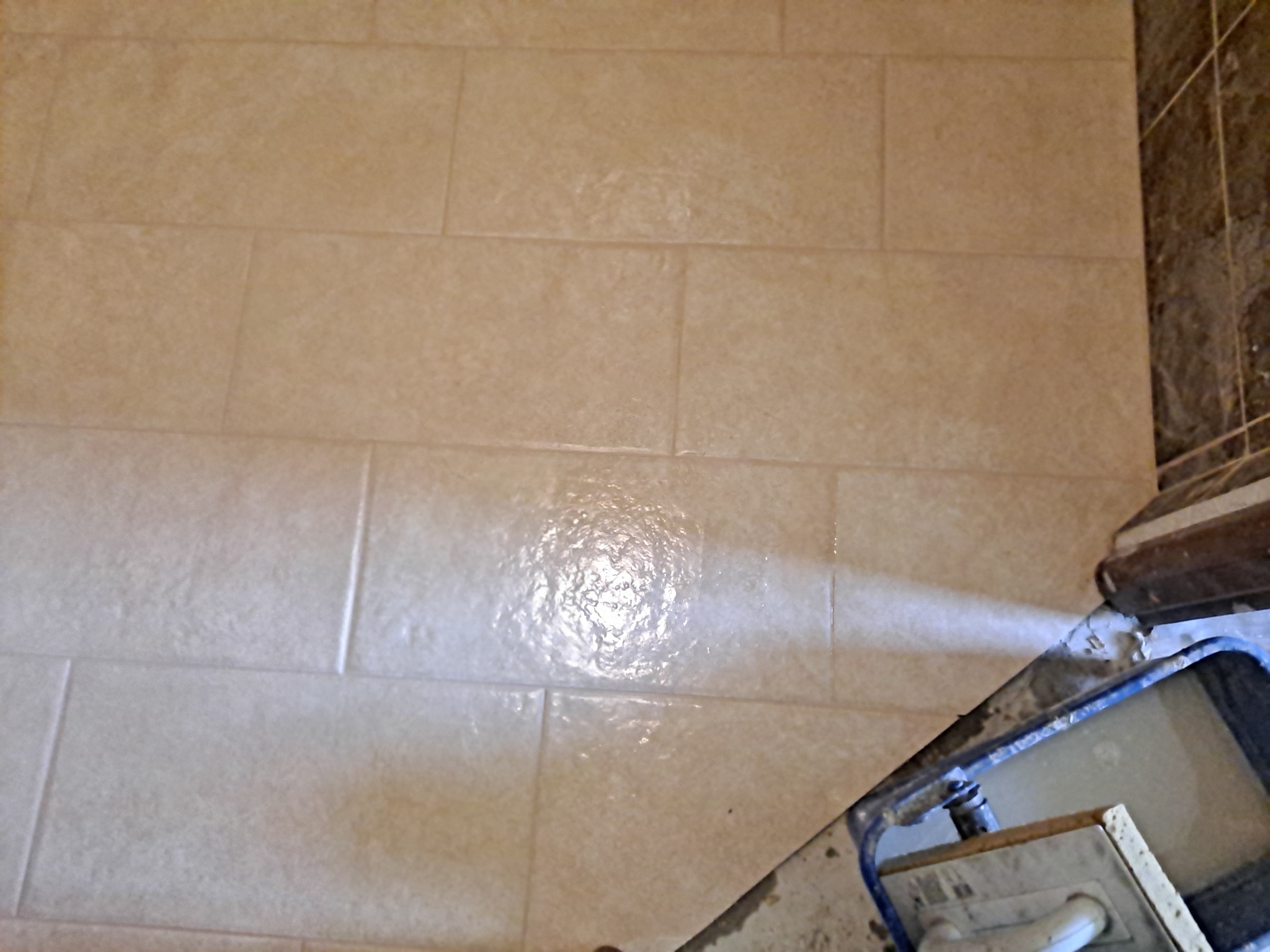 Układanie beżowych, prostokątnych płytek na podłodze, widoczny fragment narzędzia do rozprowadzania fugi i świeżo nałożona fuga na płytkach.