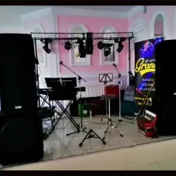 Scena z nagłośnieniem, instrumentami i oświetleniem przygotowana do występu w sali z różowymi ścianami i dekoracyjnymi łukami.