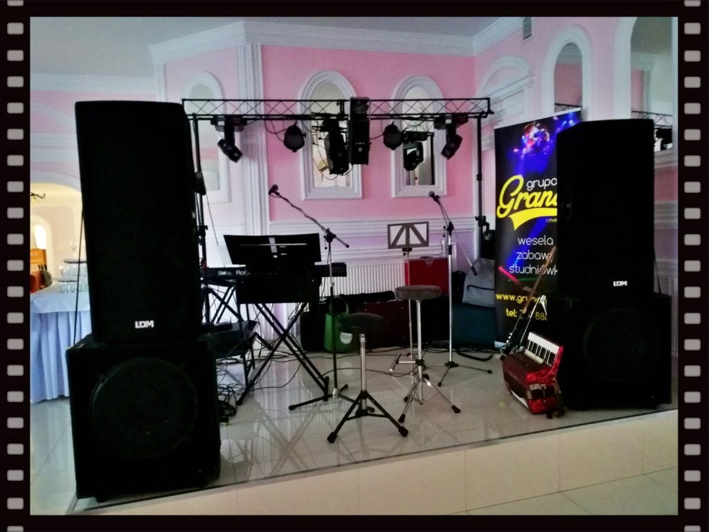 Scena z nagłośnieniem, instrumentami i oświetleniem przygotowana do występu w sali z różowymi ścianami i dekoracyjnymi łukami.
