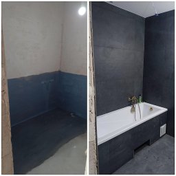 MIC-BUD - Łazienka w trakcie metamorfozy: surowy stan z hydroizolacją w strefie mokrej kontrastuje z wykończoną strefą z ciemnymi płytkami, białą wanną i złotą armaturą.