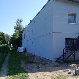 MIC-BUD - Elewacja budynku po remoncie, z widocznymi schodami zewnętrznymi i ścieżką. Jasna kolorystyka, nowoczesny styl. Ujęcie z boku, w tle zieleń.