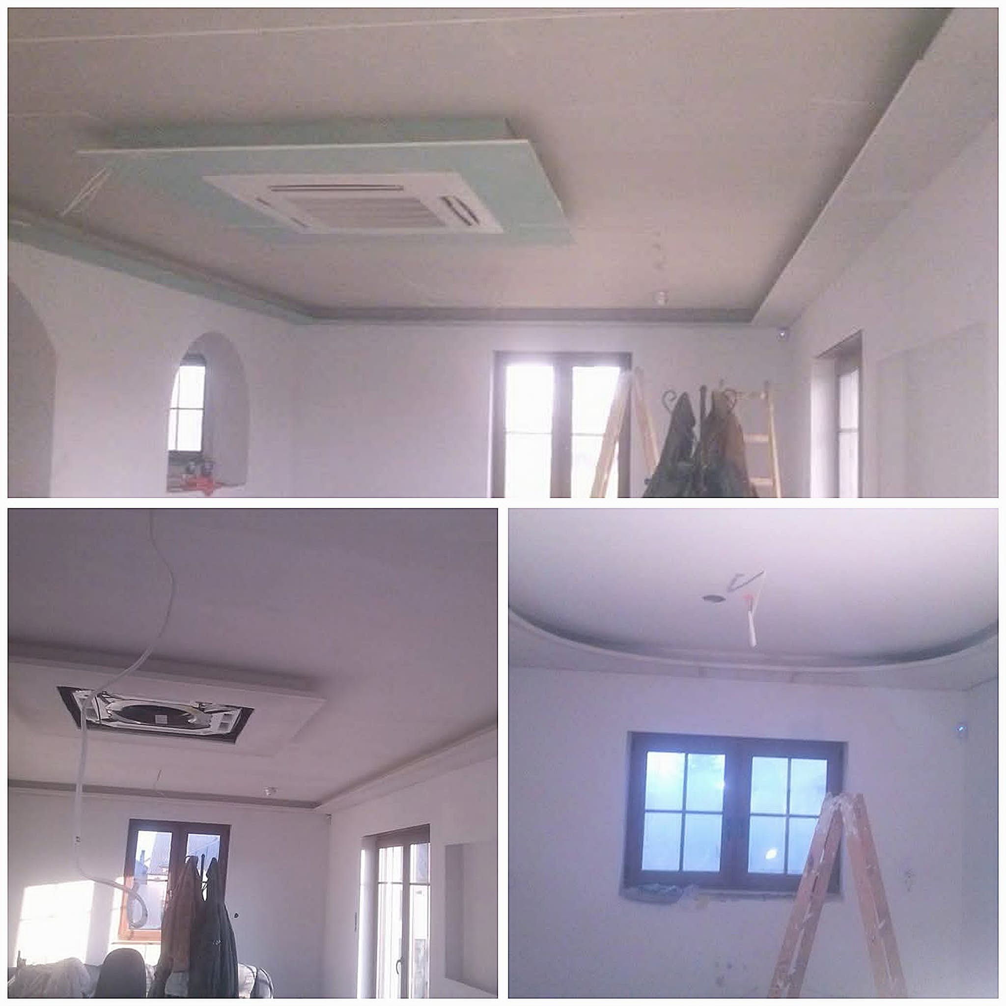 Sufit z zamontowaną klimatyzacją w obudowie z płyty karton gips, widoczne elementy wykończeniowe i drabina w pomieszczeniu z oknami.