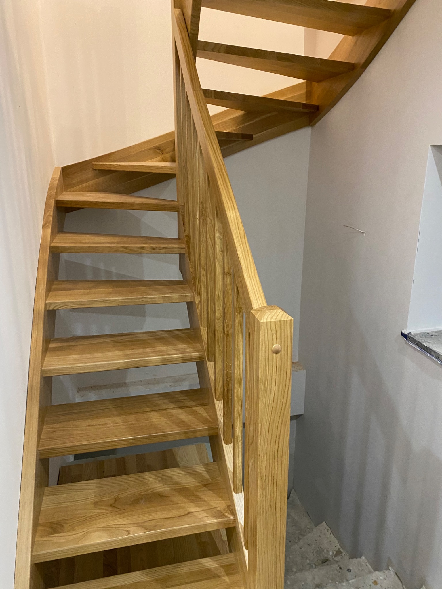 Jasne, drewniane schody z balustradą w jasnym wnętrzu podczas remontu, widoczne niedokończone ściany i schody prowadzące w dół.