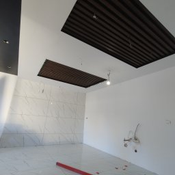 Usługi remontowe Marcin Ochałek - Wnętrze w trakcie prac wykończeniowych: płytki marmurowe na podłodze i ścianie, poziomica w kolorze czerwonym, klipsy dystansowe, dekoracyjny sufit z drewnianych listew