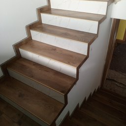 Usługi remontowe Marcin Ochałek - Schody wykończone panelami imitującymi drewno i białymi płytkami marmurowe, widoczne niedociągnięcia przy ścianie wymagające wykończenia.