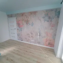 Pusty pokój po remoncie z nową tapetą w kwiaty, drewnianą podłogą i pomalowanym na jasny niebieski kolor sufitem.