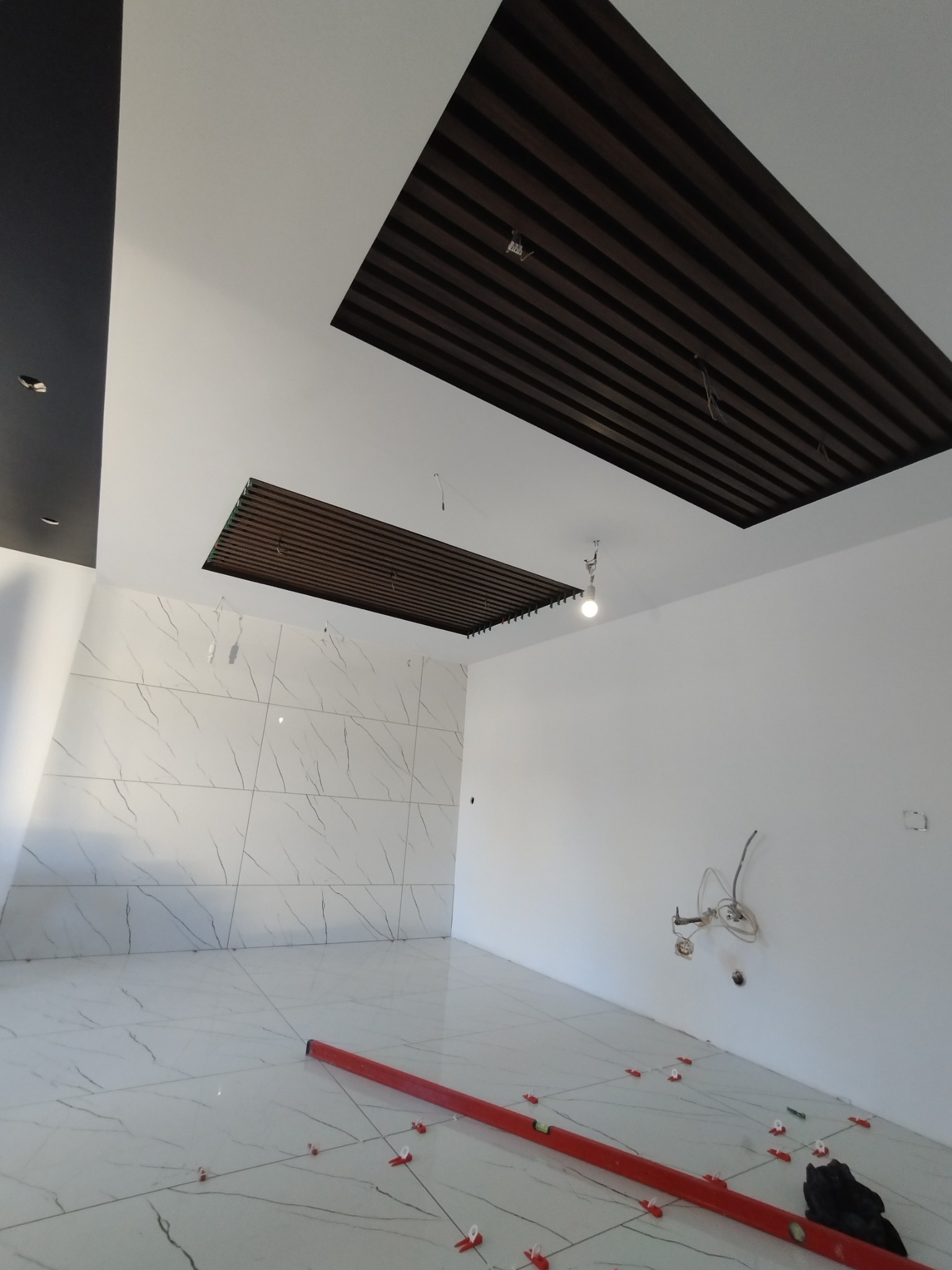 Wnętrze w trakcie prac wykończeniowych: płytki marmurowe na podłodze i ścianie, poziomica w kolorze czerwonym, klipsy dystansowe, dekoracyjny sufit z drewnianych listew