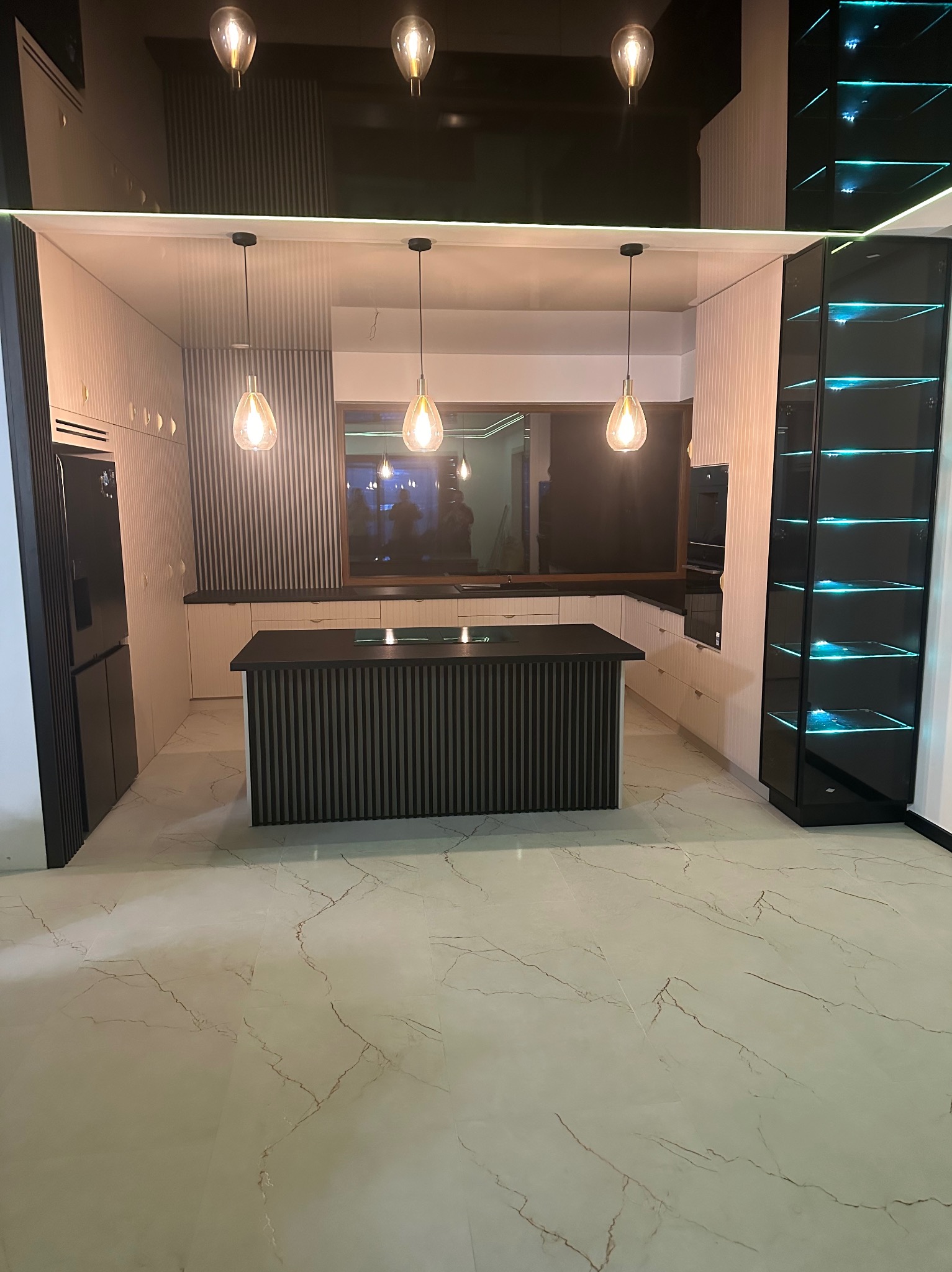Nowoczesna kuchnia z wyspą, oświetleniem punktowym i podświetlaną witryną, wykończona w bieli i czerni, z marmurową podłogą.