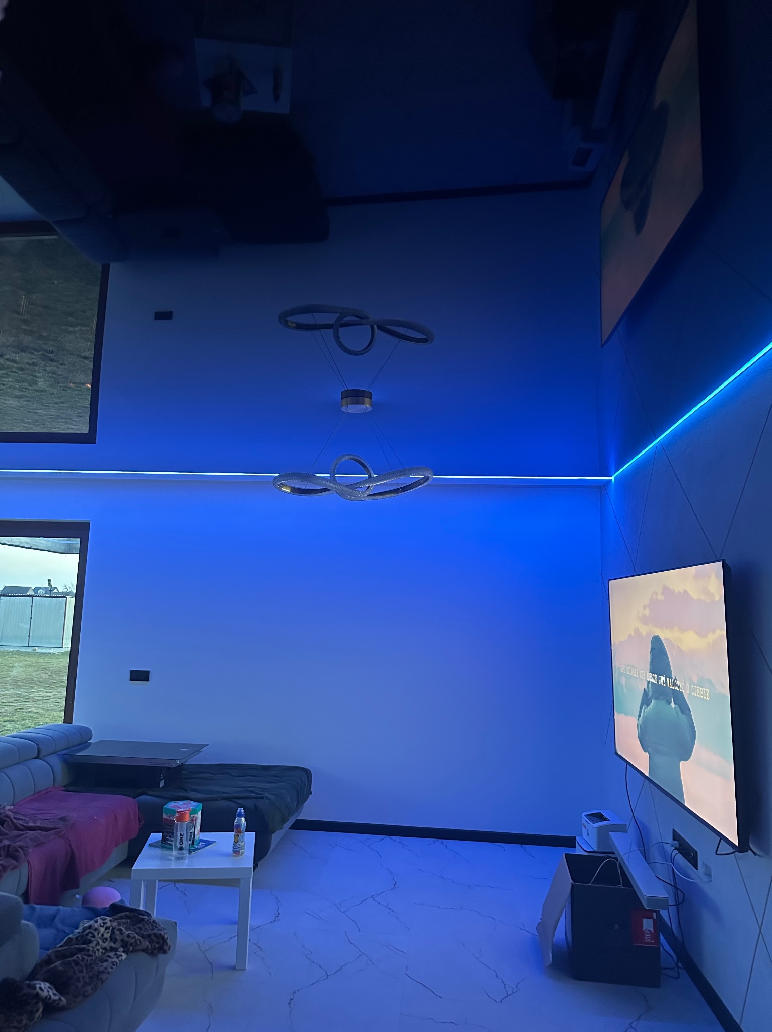 Nowoczesne wnętrze pokoju z marmurową podłogą, oświetleniem LED i designerską lampą wiszącą, całość utrzymana w chłodnej, niebieskiej tonacji.