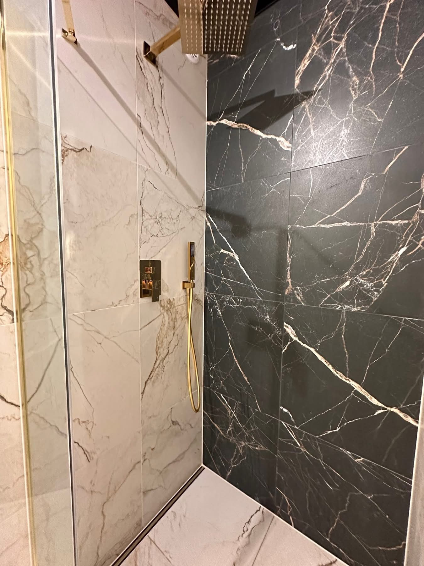 Nowoczesna kabina prysznicowa z marmurowymi płytkami w odcieniach bieli i czerni, złota armatura. Detal wykończenia łazienki z luksusowym akcentem.