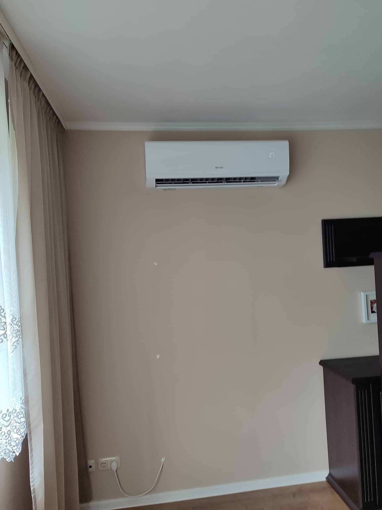 Nowoczesny klimatyzator ścienny w Gołkowicach, zamontowany nad telewizorem, z widocznym wyświetlaczem temperatury i delikatnymi, kremowymi zasłonami w tle.