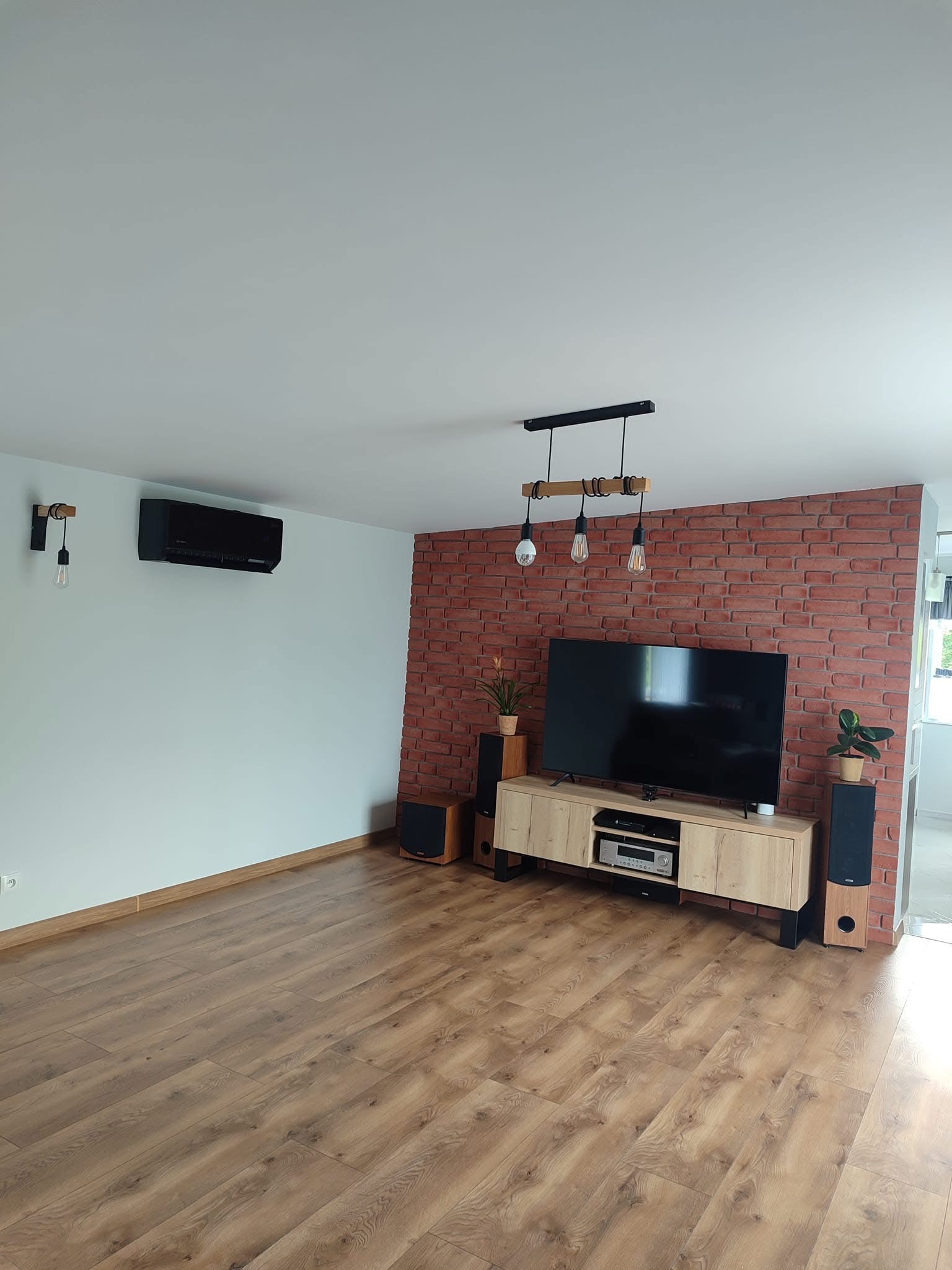 Nowoczesny salon z czarną jednostką klimatyzacyjną na ścianie, drewnianą podłogą i ścianą z czerwonej cegły