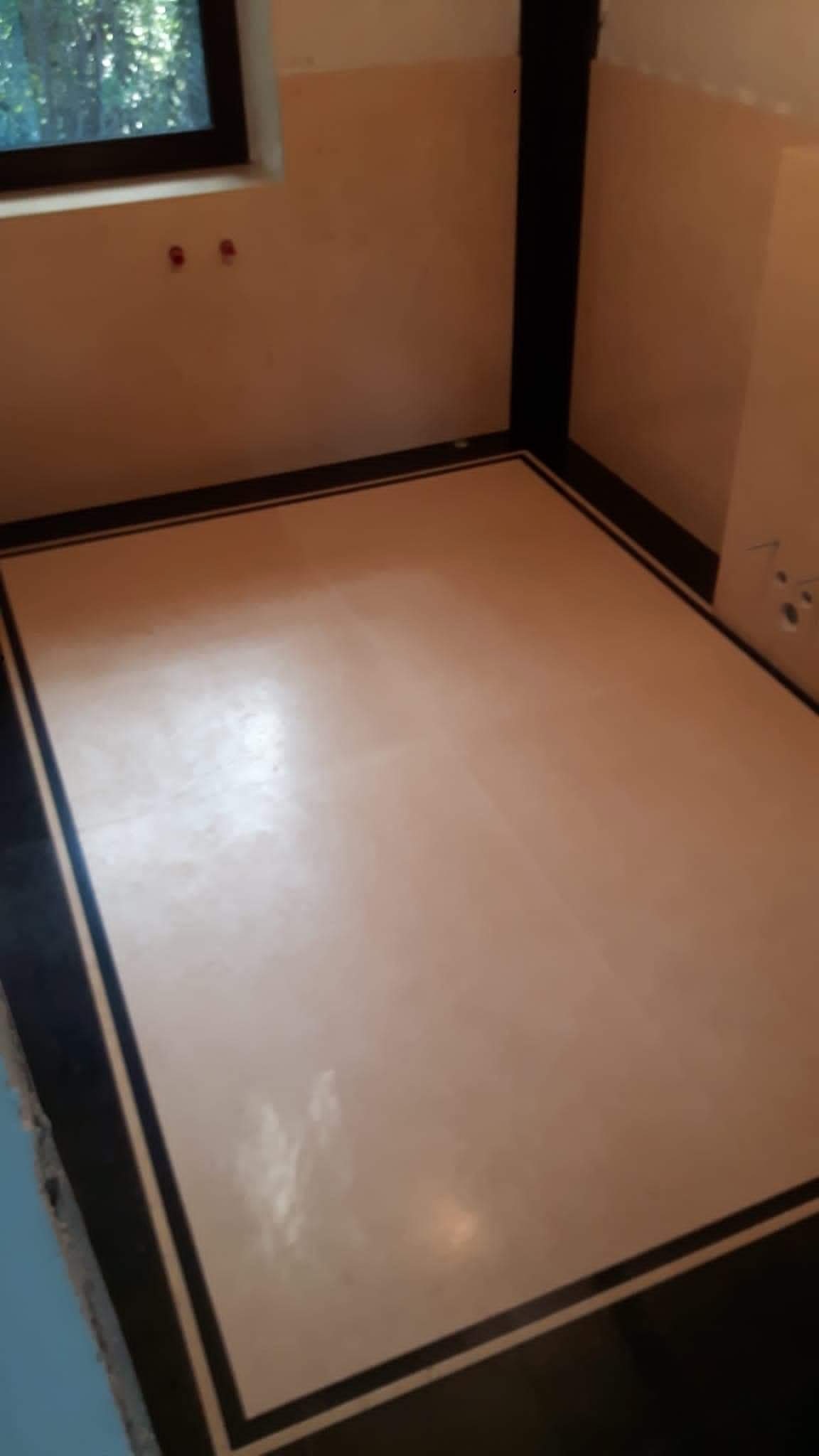 Wykończona podłoga w pokoju z czarną obwódką, świeżo po wylaniu wylewki samopoziomującej, widoczne ślady po wałku odpowietrzającym.