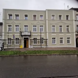 Trzypiętrowy budynek mieszkalny po renowacji elewacji, widoczne rusztowania przy balkonie, pochmurny dzień.