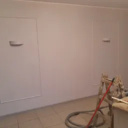 Świeżo pomalowane wnętrze z dwoma ozdobnymi panelami ściennymi z oświetleniem, drabina malarska i sprzęt do szlifowania przy ścianie.