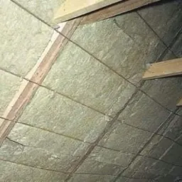 Poddasze z widoczną izolacją termiczną z wełny mineralnej, drewniana konstrukcja krokwi i niewielkie okno w tle.