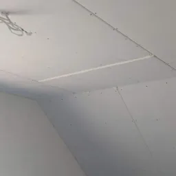 Sufit poddasza wykończony płytami kartonowo-gipsowymi, widoczne łączenia płyt i wkręty, fragment instalacji elektrycznej.